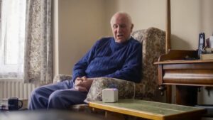 An elderly man in an armchair at home, speaking to the MiiCube - part of the MiiCare package of support.