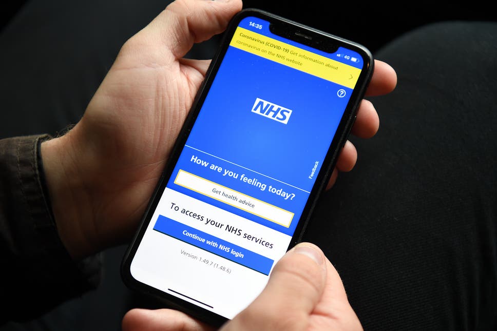 A person holding a smartphone which displays the opening screen of the NHS App.