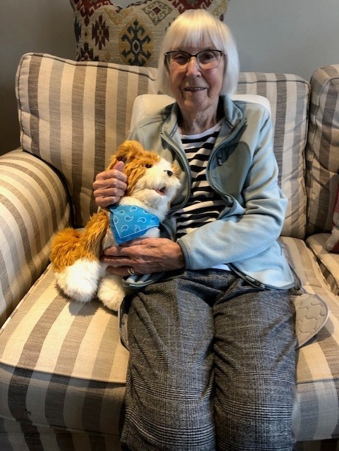 A lady with dementia, sat on a sofa with her RoboPet dog.