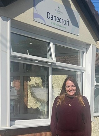 A woman is standing outside a building which has a sign which reads "Danecroft Residential Care Home" above the windows.