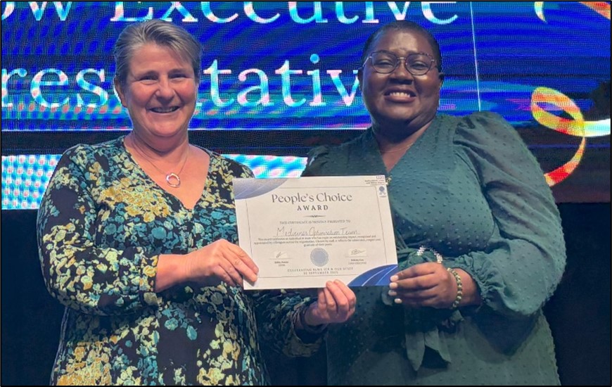Two women are smiling as one hands over a certificate to the other.